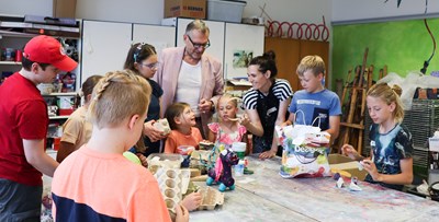 Oberbürgermeister und vhs-Vorsitzender Thomas Feser besucht das Sommerferienprogramm. Kursleiterin Stefanie Kettel zeigt, wie aus Restmaterial kleine Kunstwerke entstehen können.